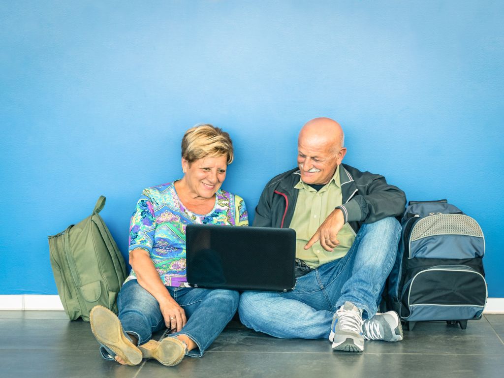 An elderly couple look at a laptop and choose to travel